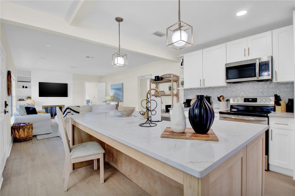 A kitchen with a large white quartz island, light wood cabinetry, and an adjacent living room — 1608 OTTAWA ROAD, CLEARWATER, FL