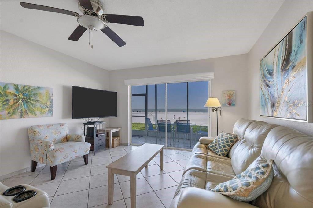 A living room features a leather sofa, patterned armchair, television, and sliding doors overlooking a beach — 6154 MIDNIGHT PASS ROAD UNIT 103, SARASOTA, FL