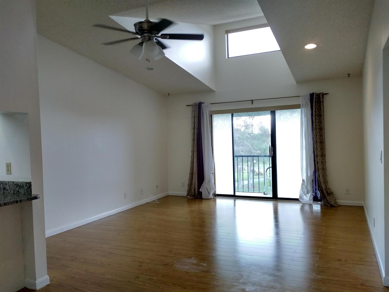 An empty living room with vaulted ceilings, a ceiling fan, hardwood floors, and sliding doors — 1113 Green Pine Boulevard # B3, West Palm Beach FL 33409, WEST PALM BEACH, FL
