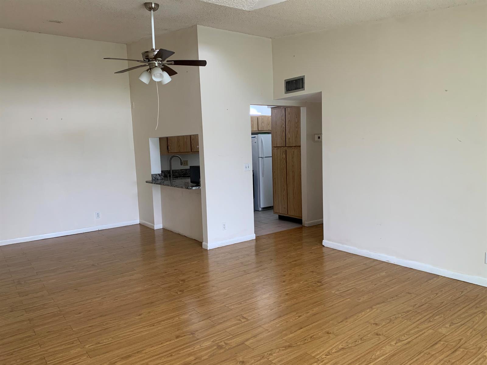An open living area features wood-look flooring, a ceiling fan, and a kitchen pass-through window — 1113 Green Pine Boulevard # B3, West Palm Beach FL 33409, WEST PALM BEACH, FL