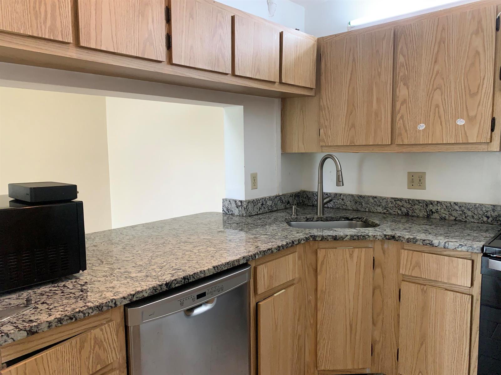 A kitchen features oak cabinets, granite countertops, a stainless steel dishwasher, and a corner sink — 1113 Green Pine Boulevard # B3, West Palm Beach FL 33409, WEST PALM BEACH, FL