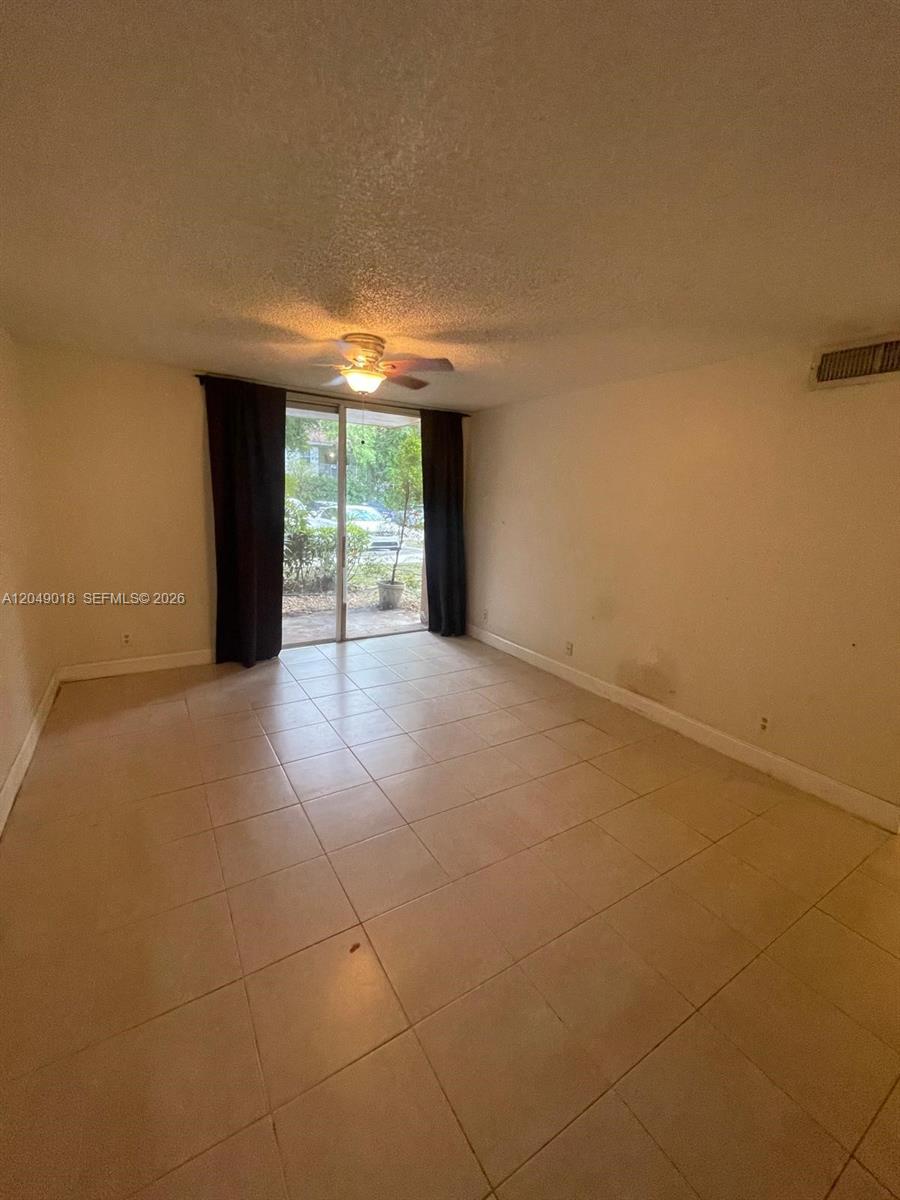 An empty room features beige tile flooring, a ceiling fan, and sliding glass patio doors — 10773 Cleary Blvd # 103, Plantation FL 33324, PLANTATION, FL