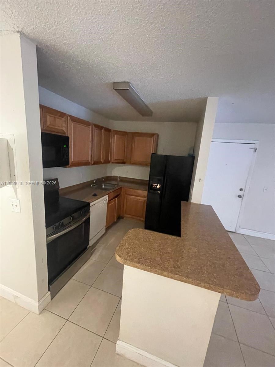A kitchen features light wood cabinets, black appliances, and a tan countertop breakfast bar — 10773 Cleary Blvd # 103, Plantation FL 33324, PLANTATION, FL