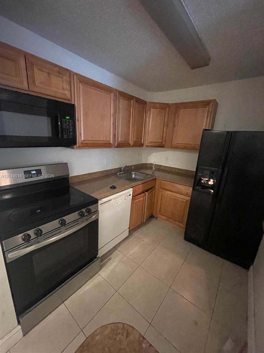 A kitchen features light wood cabinets, black appliances, a white dishwasher, and tiled flooring — 10773 Cleary Blvd # 103, Plantation FL 33324, PLANTATION, FL