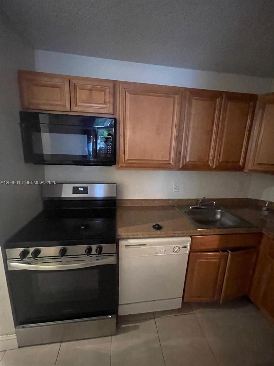 A kitchen features wood cabinets, a black microwave, a stainless steel stove, and a dishwasher — 10773 Cleary Blvd # 103, Plantation FL 33324, PLANTATION, FL