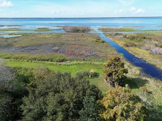 An aerial view shows a grassy field, trees, and a narrow canal leading to a lake — 4705 KISSIMMEE PARK ROAD, ST CLOUD, FL