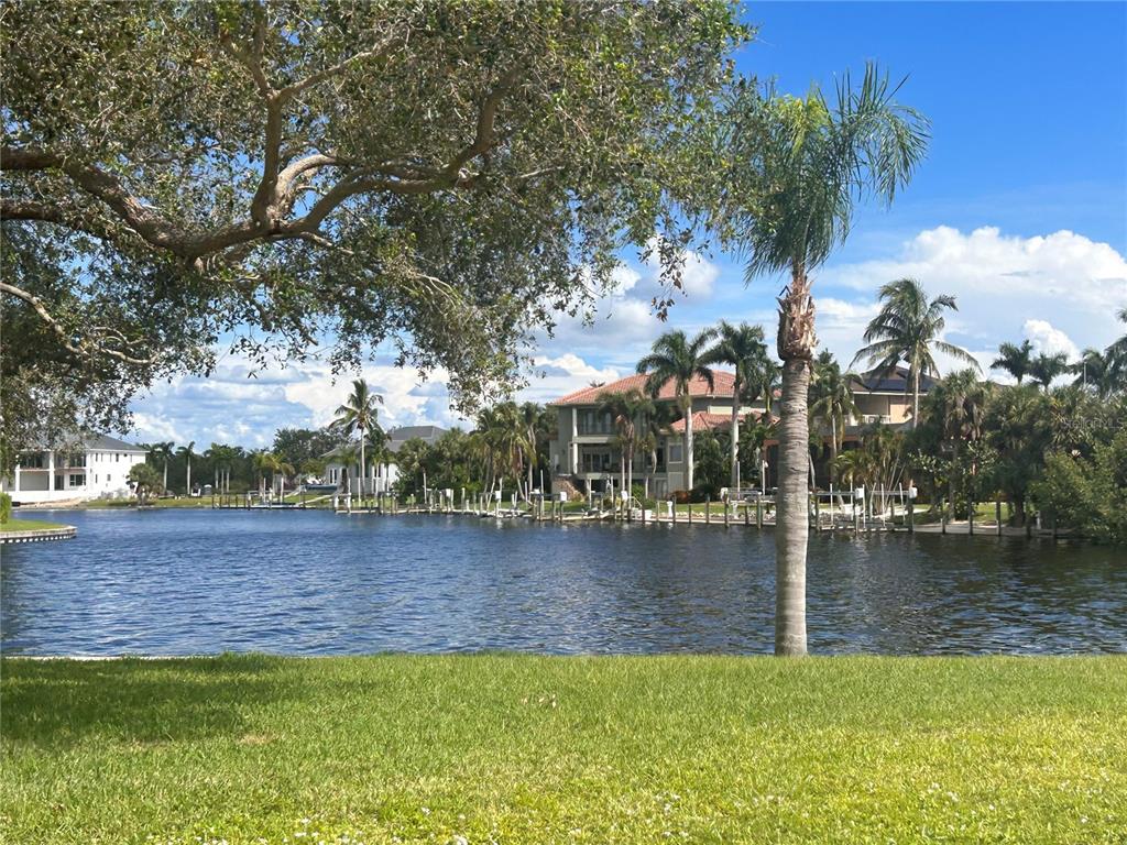 A view of a canal with houses, docks, palm trees, and a grassy lawn — 143 CREEK DRIVE SE, PORT CHARLOTTE, FL