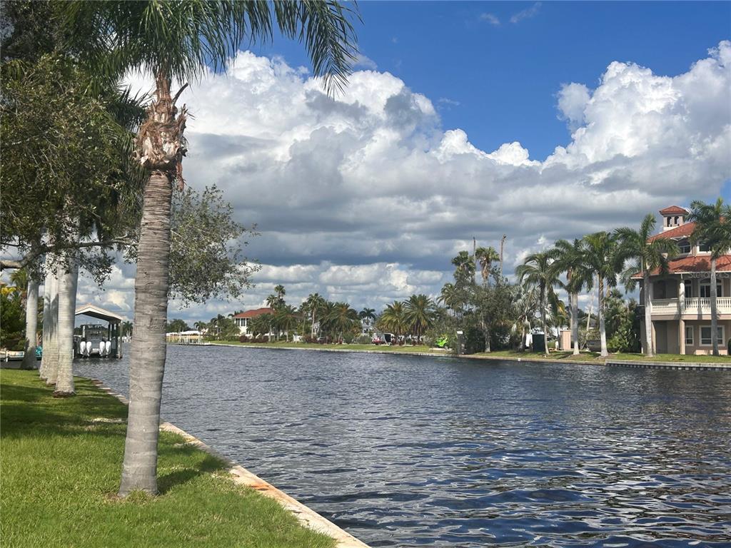 A view of a canal lined with palm trees, green lawns, and waterfront houses — 143 CREEK DRIVE SE, PORT CHARLOTTE, FL