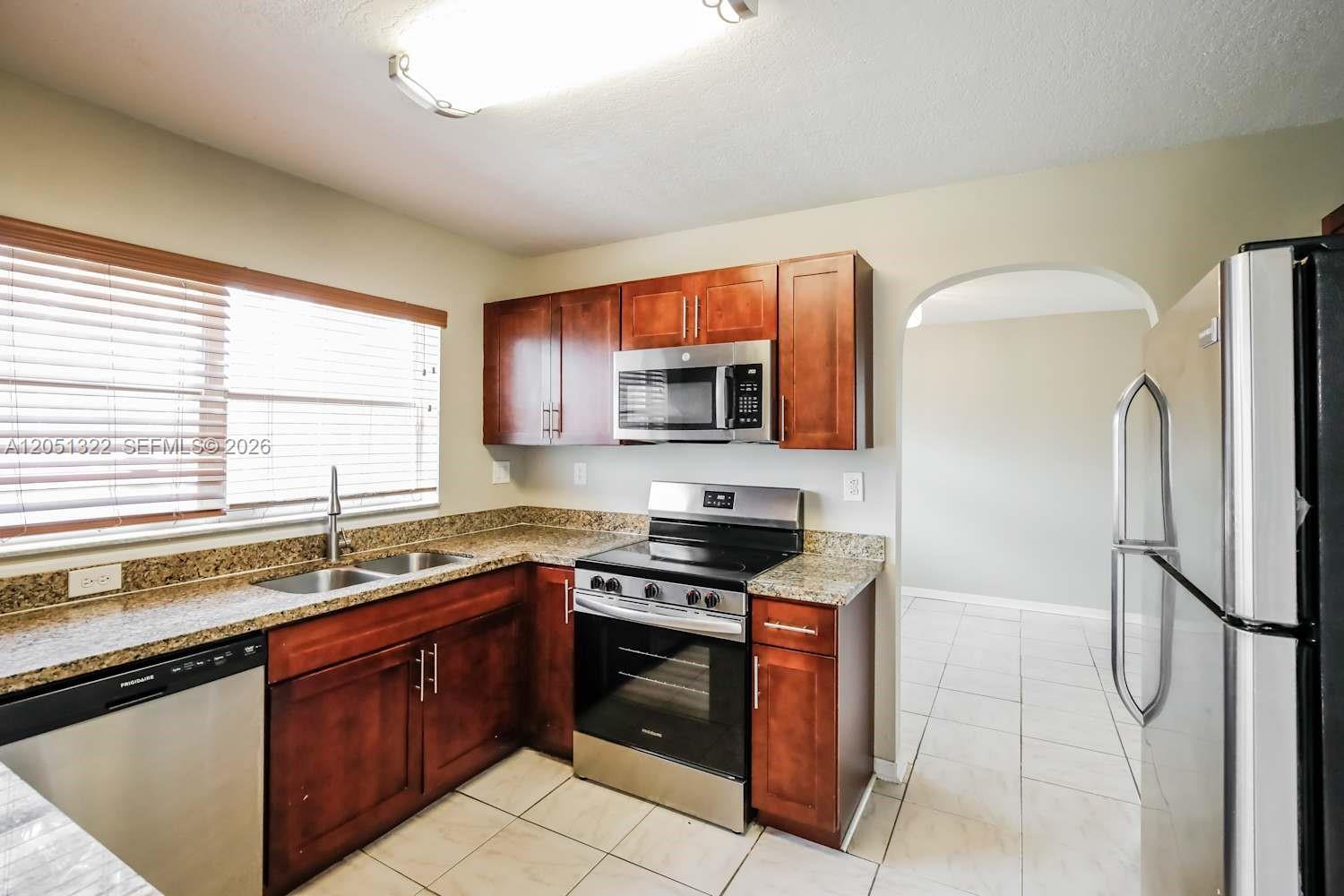 A kitchen features wood cabinets, granite countertops, stainless steel appliances, and tile flooring — PEMBROKE PINES, FL