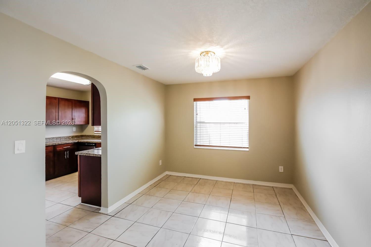 A dining area with beige walls, tile flooring, a crystal light fixture, and an arched doorway — PEMBROKE PINES, FL