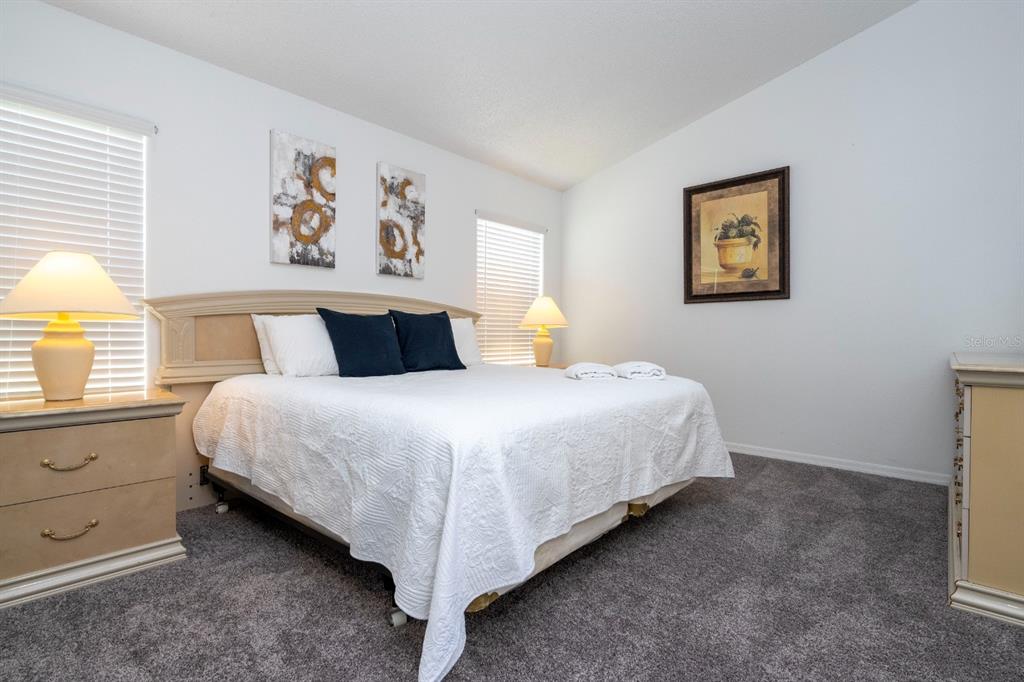 A bedroom features a king bed with white bedding, two nightstands, and gray carpeting — 4669 PRAIRIE POINT BOULEVARD, KISSIMMEE, FL