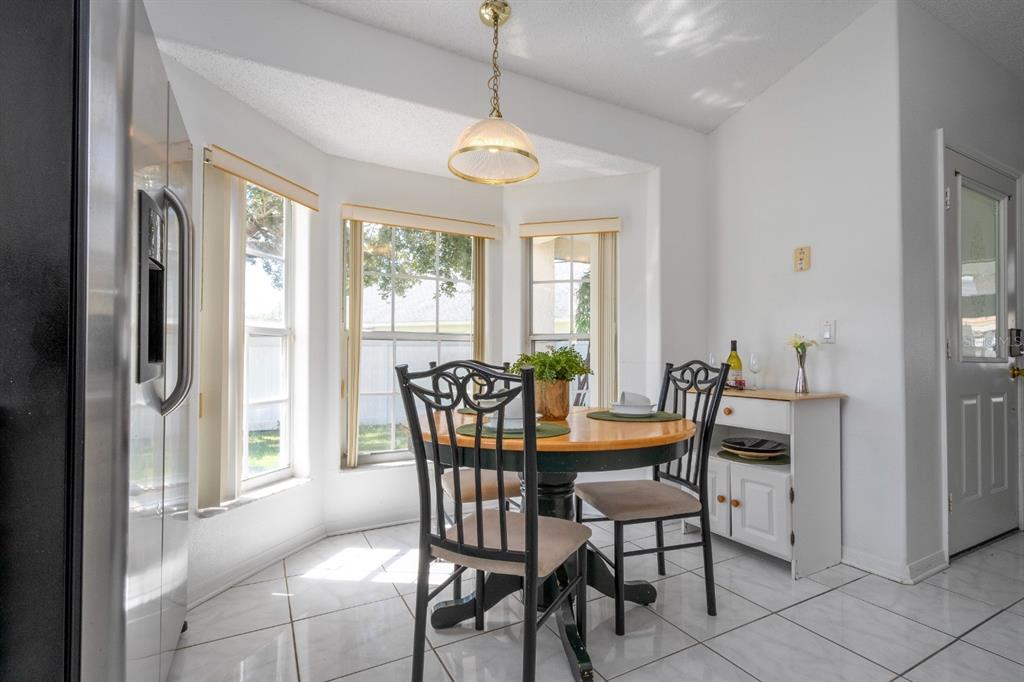 A bright breakfast nook features a round wooden table, black chairs, and white tile flooring — 4669 PRAIRIE POINT BOULEVARD, KISSIMMEE, FL