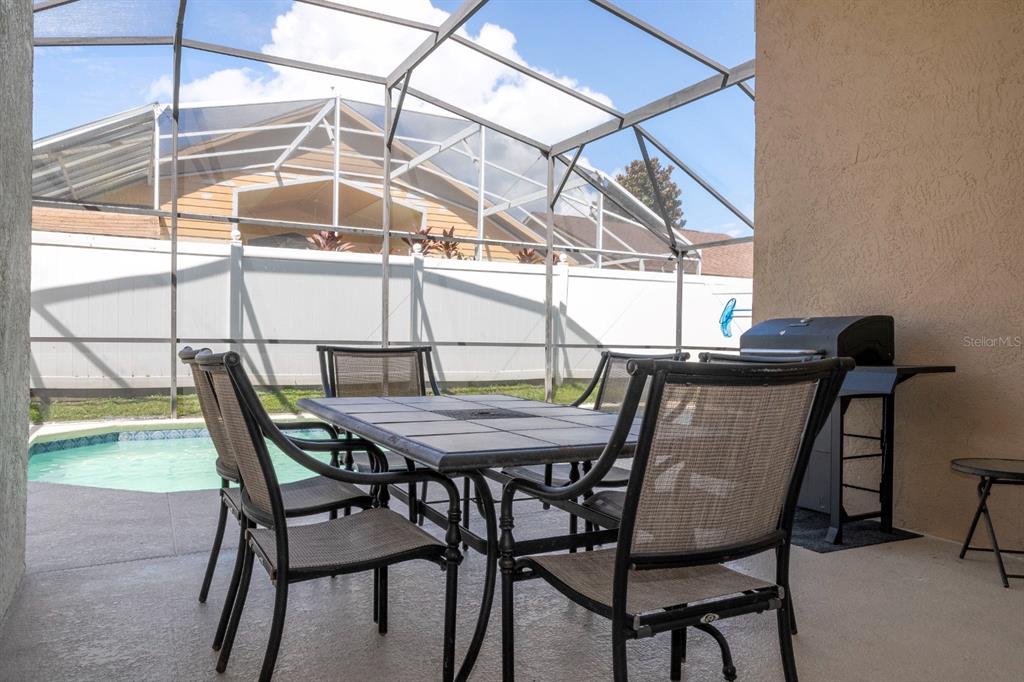 A screened-in patio features a dining set, a grill, and a view of a pool — 4669 PRAIRIE POINT BOULEVARD, KISSIMMEE, FL