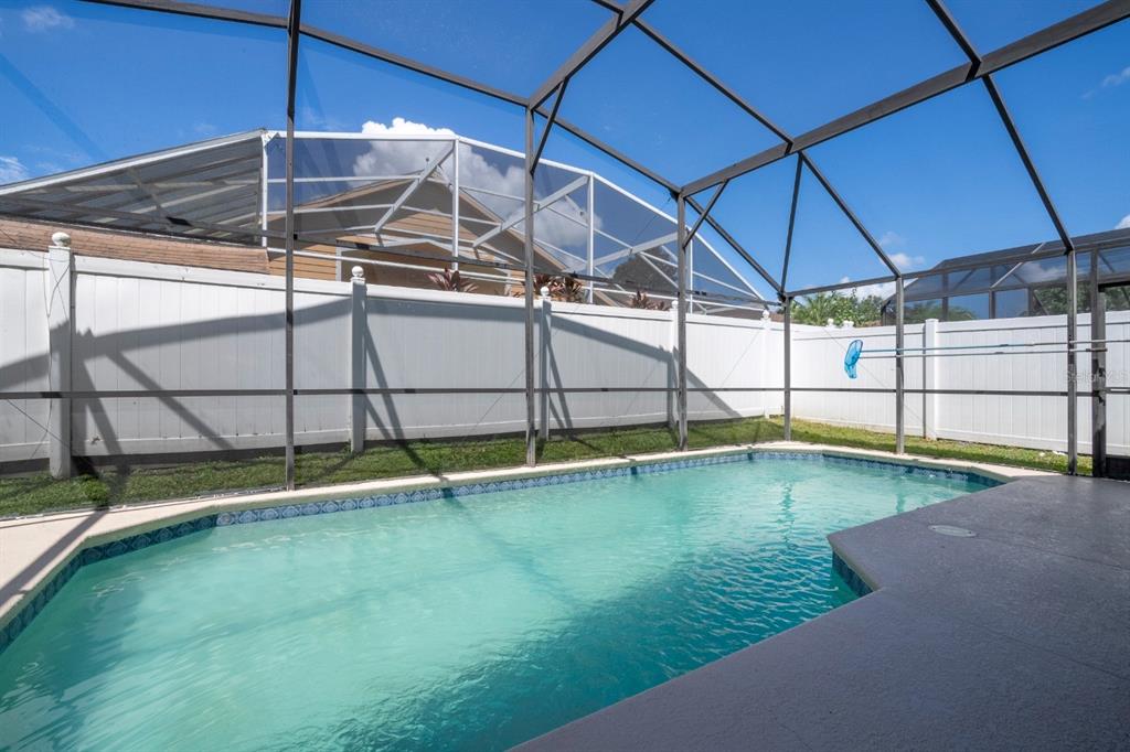 A swimming pool enclosed by a screened lanai sits in front of a white vinyl fence — 4669 PRAIRIE POINT BOULEVARD, KISSIMMEE, FL