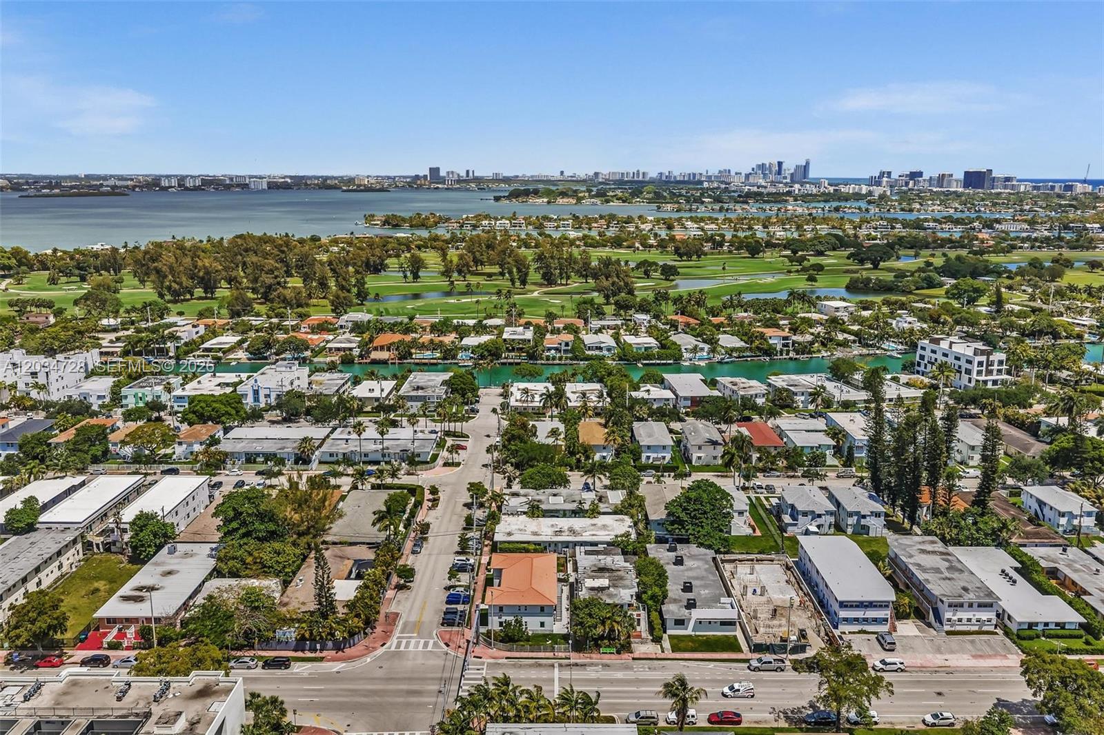 An aerial view shows a residential neighborhood with a canal, golf course, and distant skyline — 1795 Calais Dr, Miami Beach FL 33141, MIAMI BEACH, FL