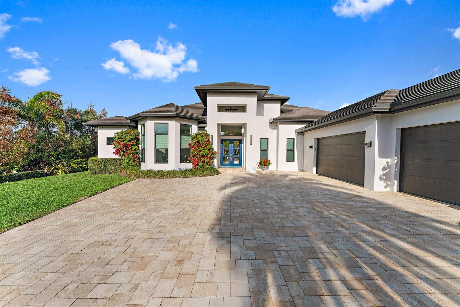 A modern white house with a paver driveway, blue double doors, and a three-car garage — 17560 SE Conch Bar Avenue, Jupiter FL 33469, JUPITER, FL