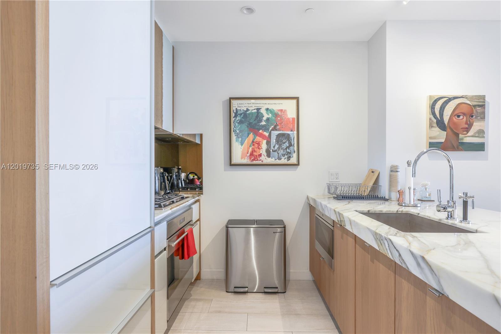A modern kitchen features light wood cabinetry, marble countertops, stainless steel appliances, and two paintings — 2831 S Bayshore Dr # 603, Miami FL 33133, MIAMI, FL