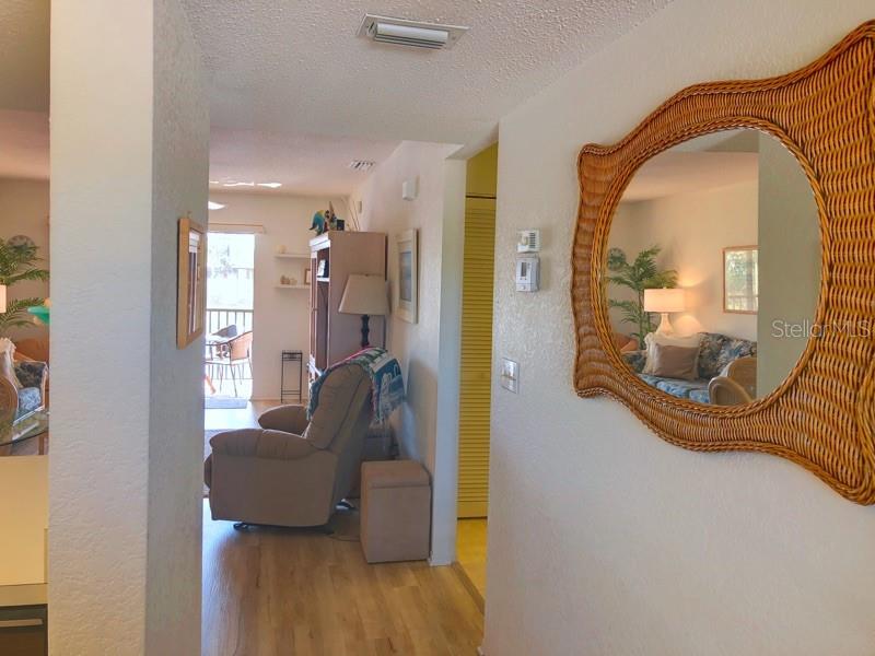 A hallway with light wood flooring leads to a living area with a recliner and balcony — 4024 OAKVIEW DRIVE UNIT I9, PORT CHARLOTTE, FL