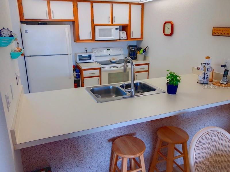 A kitchen features white appliances, wooden cabinets, a breakfast bar, and two wooden stools — 4024 OAKVIEW DRIVE UNIT I9, PORT CHARLOTTE, FL