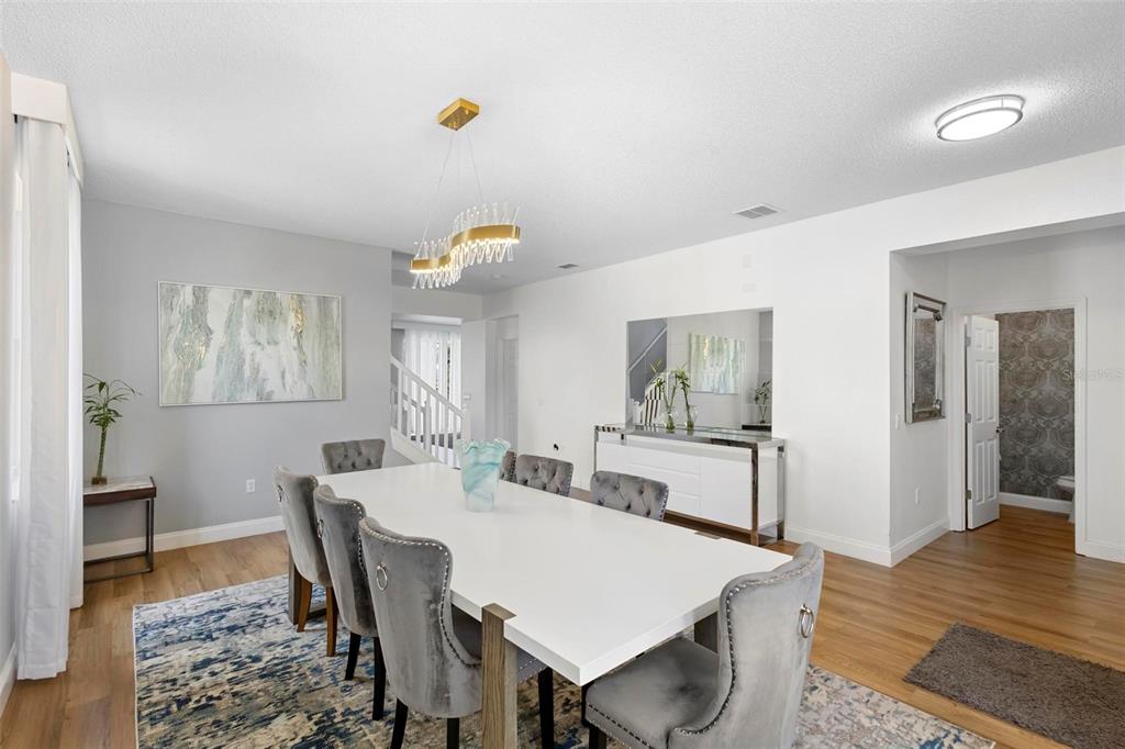 A dining room features a white table, grey tufted chairs, and a modern gold chandelier — 4539 PHILADELPHIA CIRCLE, KISSIMMEE, FL