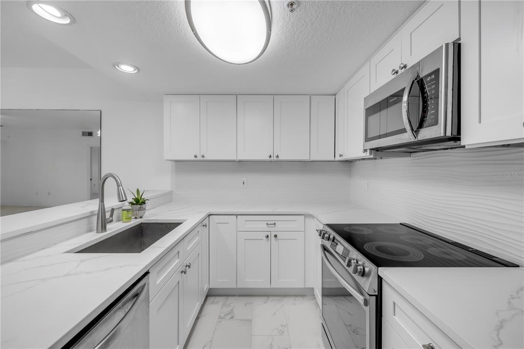 A modern kitchen features white cabinets, stainless steel appliances, and white marble-look countertops — 5300 S ATLANTIC AVENUE UNIT 1-205, NEW SMYRNA BEACH, FL