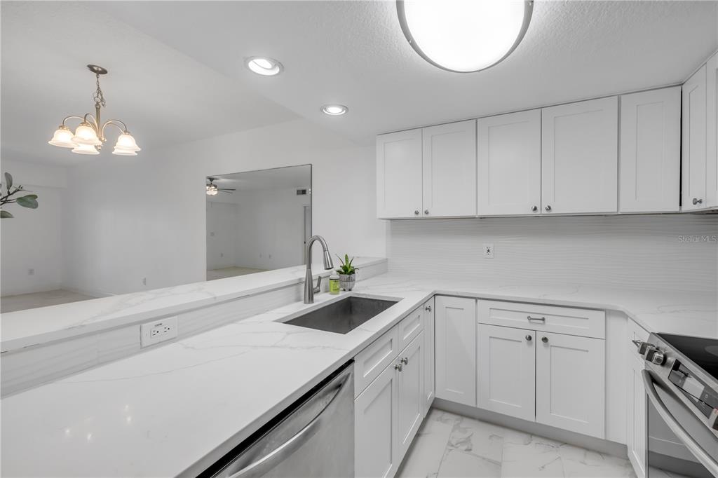 A kitchen features white cabinets, marble-look countertops, a stainless steel sink, and recessed lighting — 5300 S ATLANTIC AVENUE UNIT 1-205, NEW SMYRNA BEACH, FL