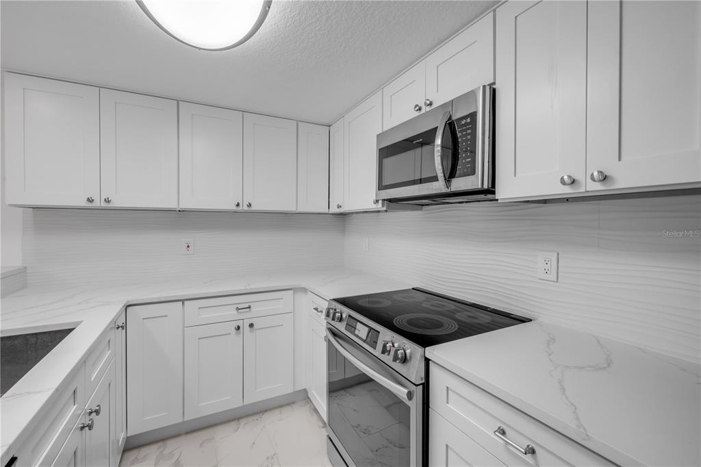 A modern kitchen features white shaker cabinets, marble-look countertops, and stainless steel appliances — 5300 S ATLANTIC AVENUE UNIT 1-205, NEW SMYRNA BEACH, FL