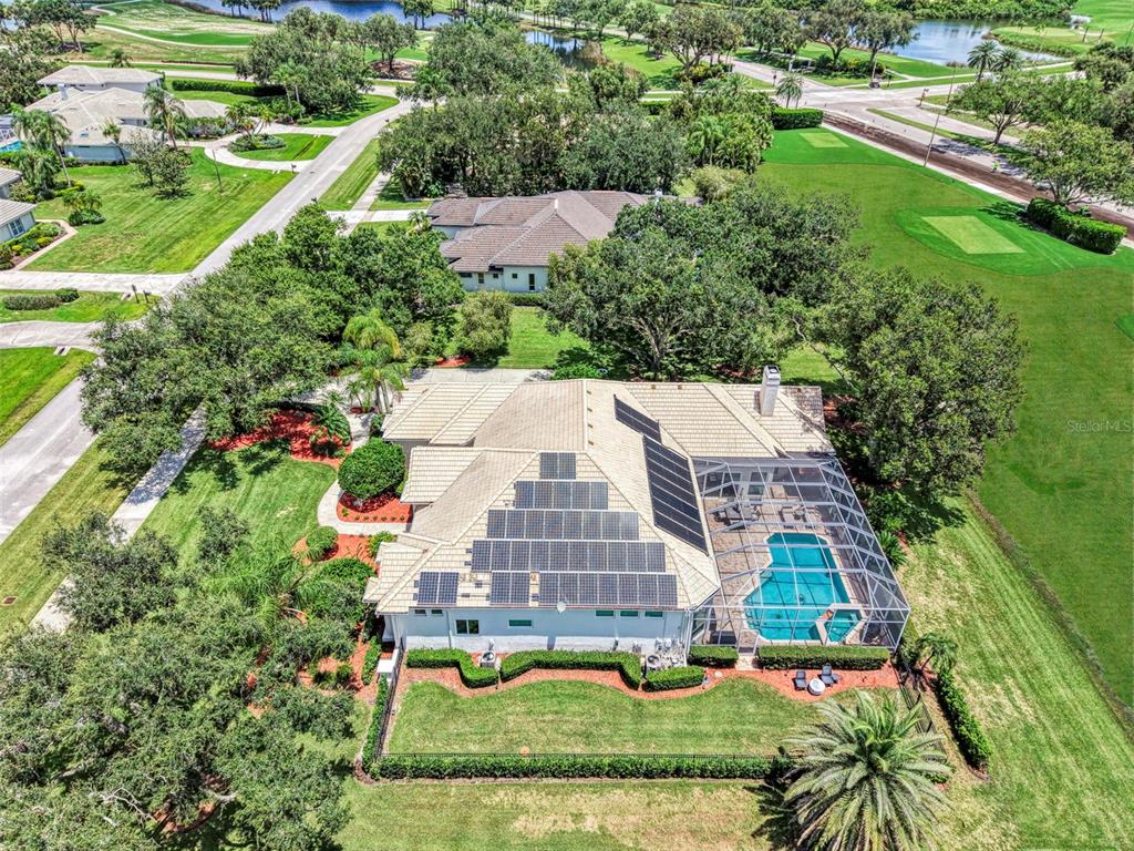 An aerial view of a house with solar panels, a screened pool, and a golf course — 7767 ALISTER MACKENZIE DRIVE, SARASOTA, FL