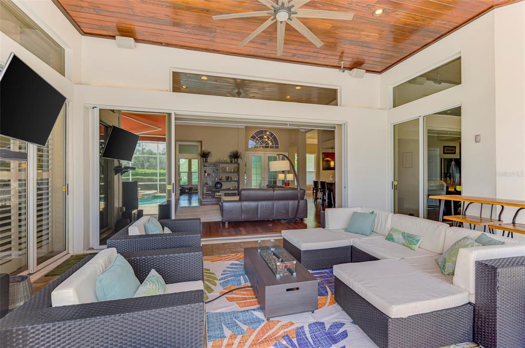 A covered outdoor patio features wicker furniture, a fire pit table, and a wood-paneled ceiling — 7767 ALISTER MACKENZIE DRIVE, SARASOTA, FL