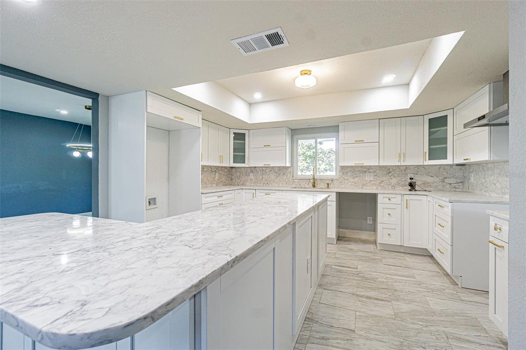 A modern kitchen features white cabinetry, marble-patterned countertops, stainless steel appliances, and gray tile flooring — 6370 CONNIEWOOD SQUARE, NEW PORT RICHEY, FL