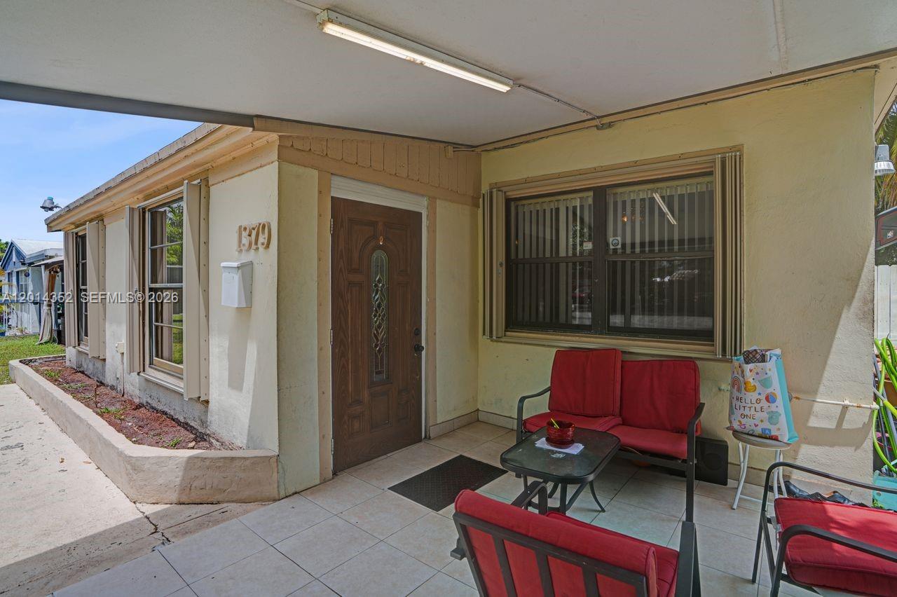 A covered front porch features a tiled floor, a wooden door, and outdoor seating furniture — 1379 NE 177th St, North Miami Beach FL 33162, NORTH MIAMI BEACH, FL