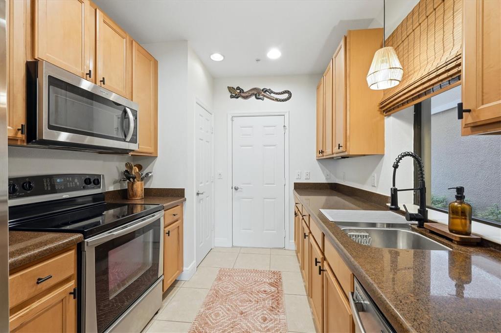 A galley kitchen features light wood cabinets, brown granite countertops, and stainless steel appliances — 7210 HAMILTON ROAD, BRADENTON, FL