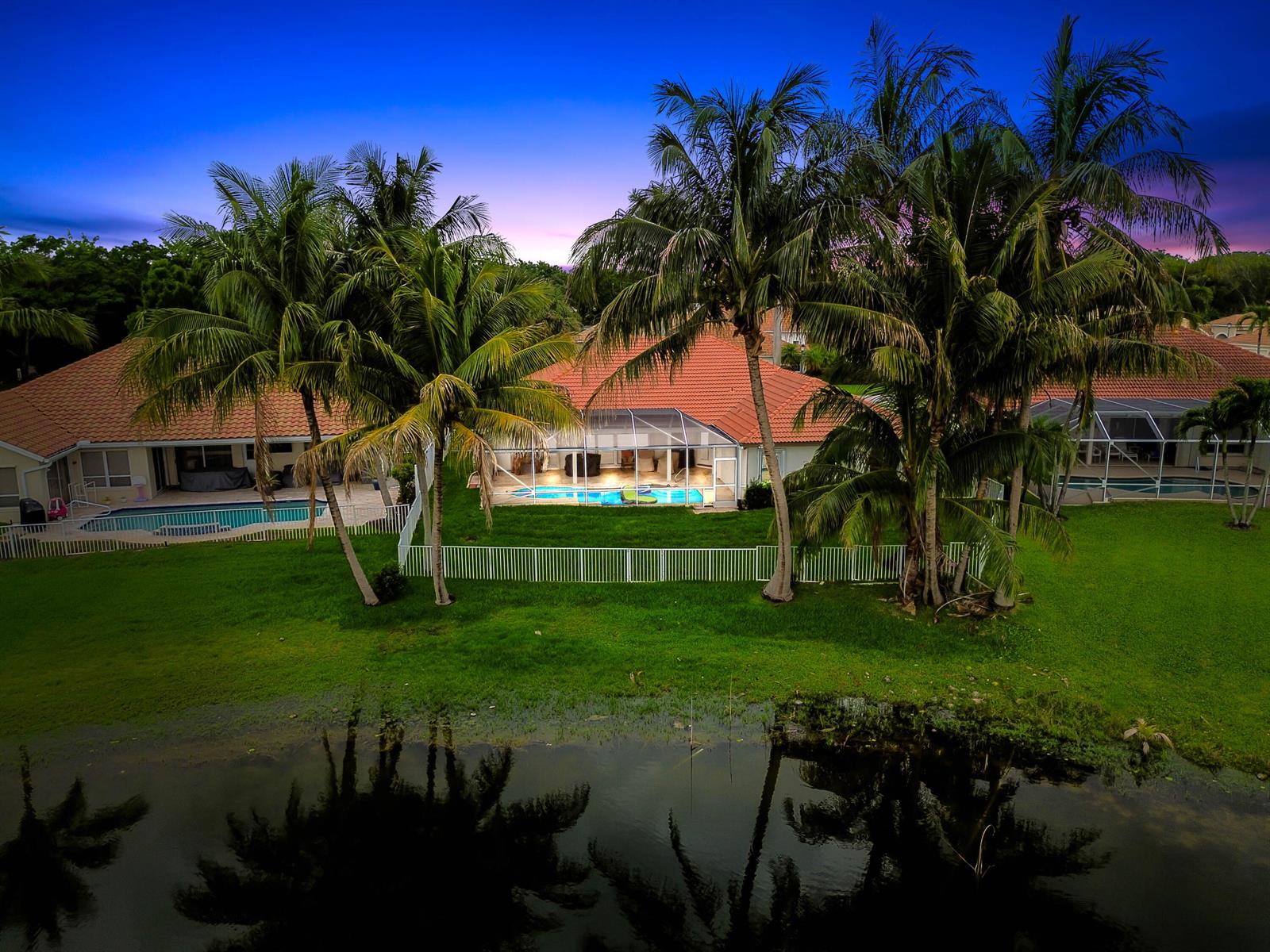 An aerial view of a house with a screened-in pool, palm trees, and a backyard pond — 7734 Belmont Drive, Lake Worth FL 33467, LAKE WORTH, FL