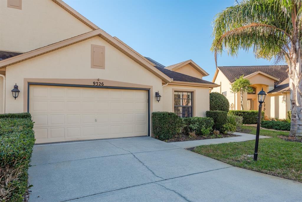 A beige house exterior features a two-car garage, a concrete driveway, and a palm tree — 9326 PALM HAVEN COURT, NEW PORT RICHEY, FL