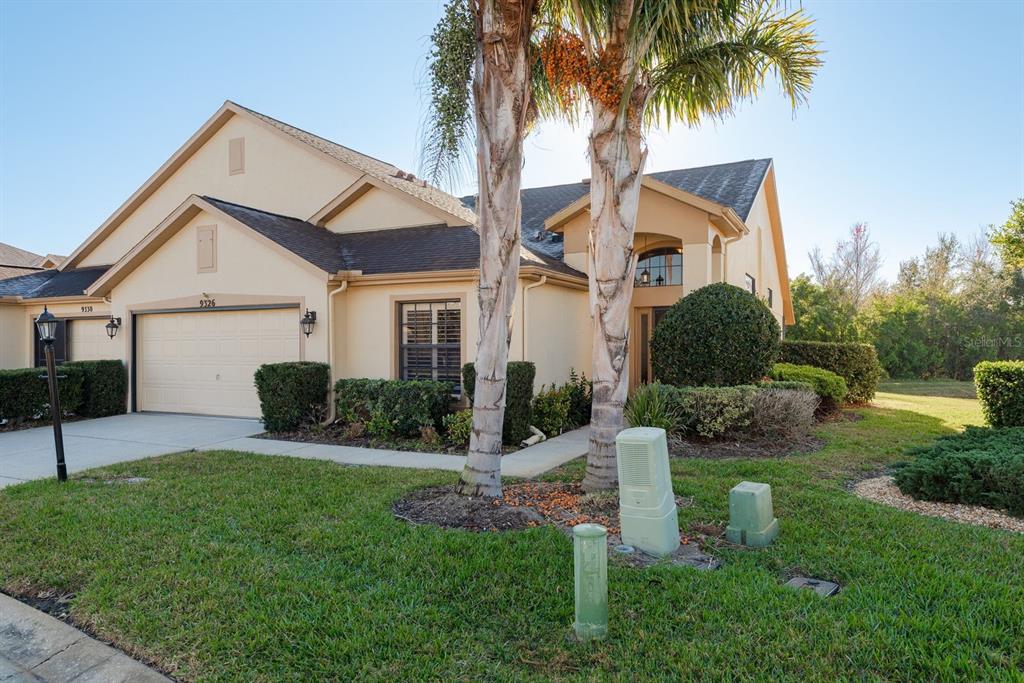 A tan, single-story house with a two-car garage and palm trees in the front yard — 9326 PALM HAVEN COURT, NEW PORT RICHEY, FL