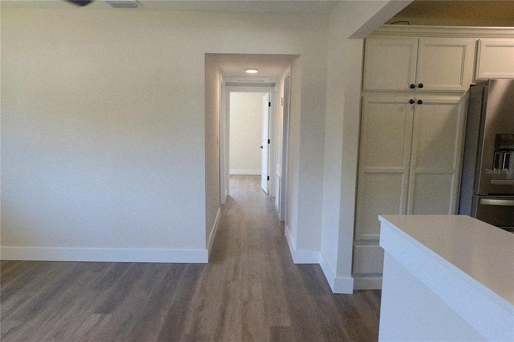A hallway with light wood-look flooring leads to a doorway in a white-walled interior — 2709 ARC DRIVE, ORLANDO, FL