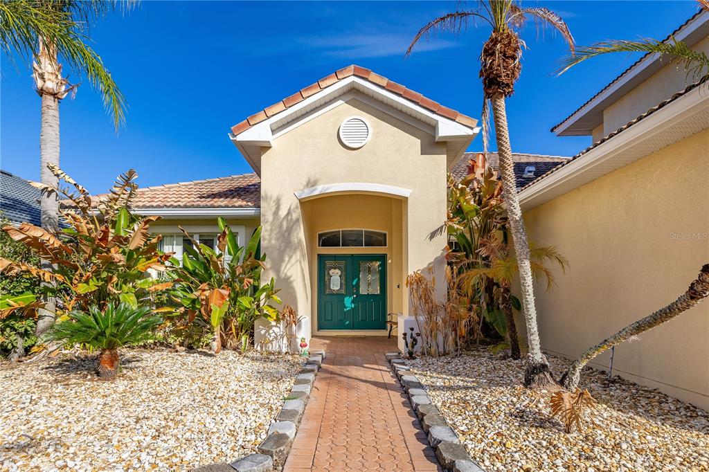A beige house exterior features a brick walkway leading to a green double front door — 1831 WINDWARD OAKS COURT, KISSIMMEE, FL