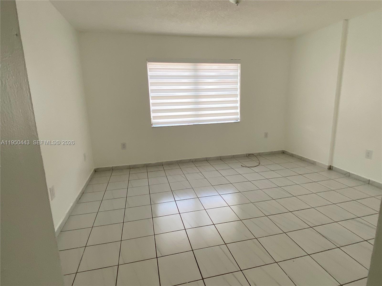 An empty room features white walls, light-colored tiled flooring, and a window with blinds — 295 NW 72nd Ave # 304, Miami FL 33126, MIAMI, FL
