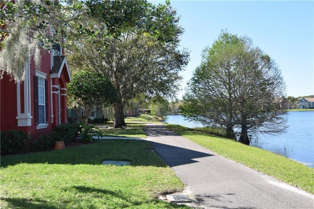 A paved path runs between a red house and a lake with large trees — 9640 LAKE CHASE ISLAND WAY, TAMPA, FL