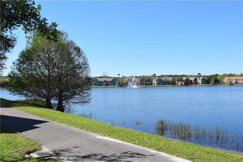 A paved path runs alongside a lake with a fountain and apartment buildings in the background — 9640 LAKE CHASE ISLAND WAY, TAMPA, FL