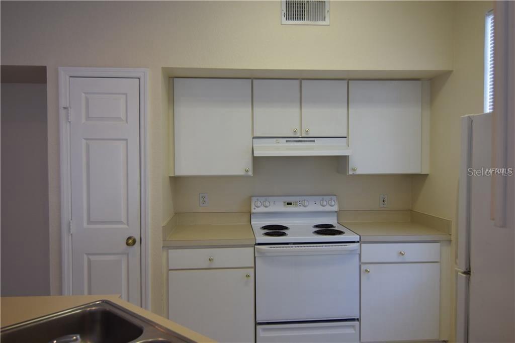 A kitchen features white cabinets, a white electric stove, and beige countertops — 9640 LAKE CHASE ISLAND WAY, TAMPA, FL