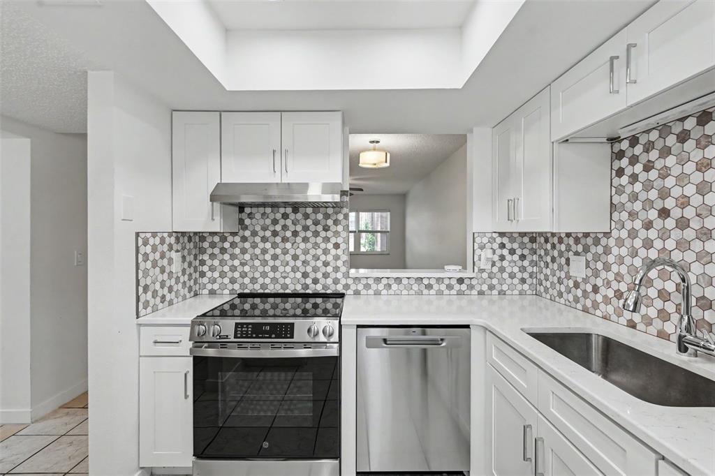 A kitchen features white cabinets, stainless steel appliances, and a hexagonal tile backsplash — 4805 ALT 19 UNIT 114, PALM HARBOR, FL