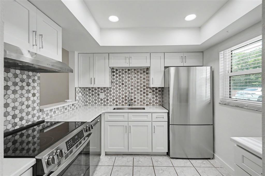 A kitchen featuring white cabinets, stainless steel appliances, and a hexagonal tile backsplash — 4805 ALT 19 UNIT 114, PALM HARBOR, FL