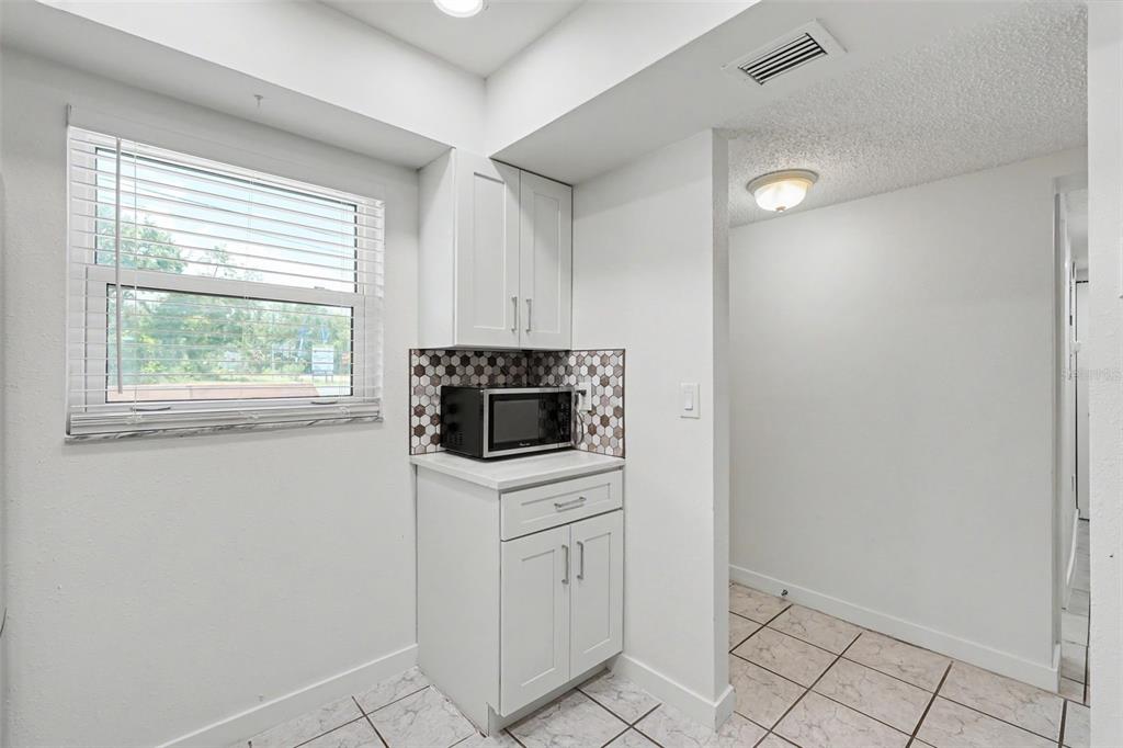 A small kitchen area features white cabinets, a microwave, and a tiled backsplash — 4805 ALT 19 UNIT 114, PALM HARBOR, FL