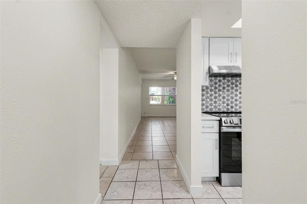A view from a hallway looking toward a kitchen with white cabinets and tiled floors — 4805 ALT 19 UNIT 114, PALM HARBOR, FL