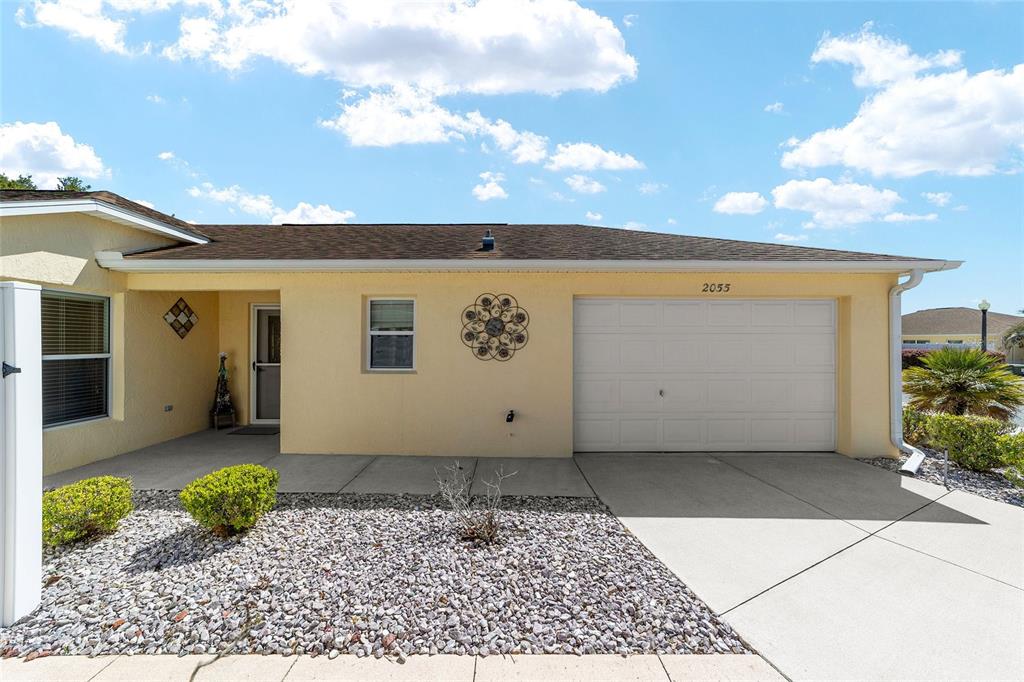 A single-story house with a yellow stucco exterior, a garage, and a gravel front yard — 2055 HYDRANGEA AVENUE, THE VILLAGES, FL