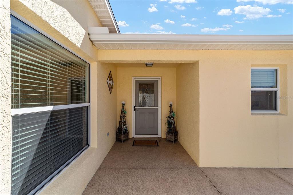 A covered entryway features a light yellow stucco exterior, a front door, and two decorative planters — 2055 HYDRANGEA AVENUE, THE VILLAGES, FL
