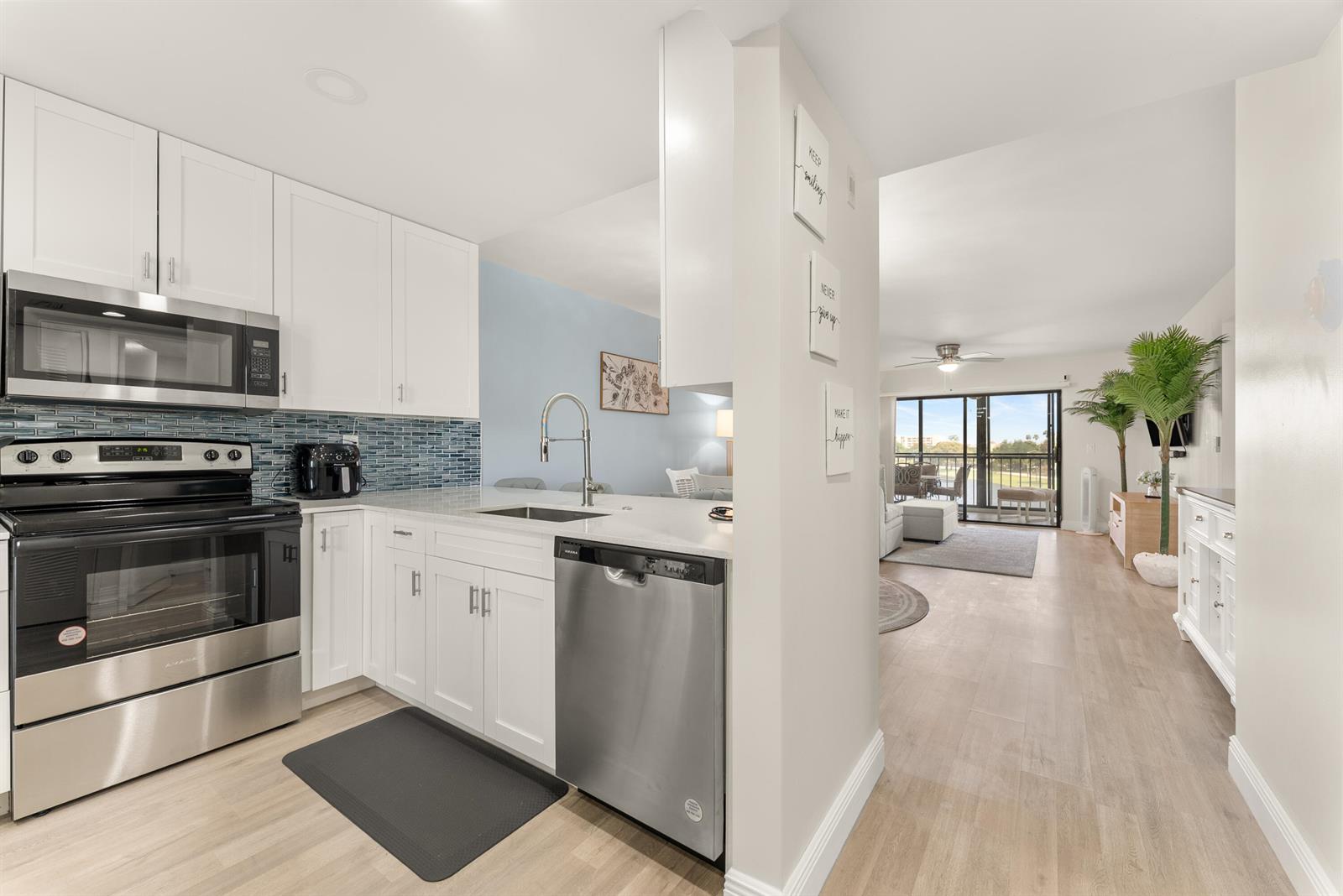 A kitchen with white cabinets and stainless steel appliances opens into a bright living area — 14500 Stirling Way # 403, Delray Beach FL 33446, DELRAY BEACH, FL