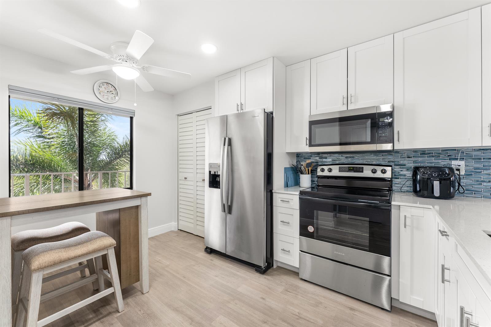 A kitchen with white cabinets, stainless steel appliances, a breakfast bar, and a window view — 14500 Stirling Way # 403, Delray Beach FL 33446, DELRAY BEACH, FL