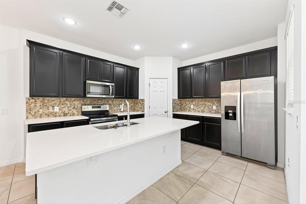 A kitchen features dark cabinets, stainless steel appliances, a white island, and a tiled backsplash — 15523 WILLOW ARBOR CIRCLE, ORLANDO, FL
